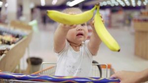a 2 year old holding bananas sitting in the shopping cart