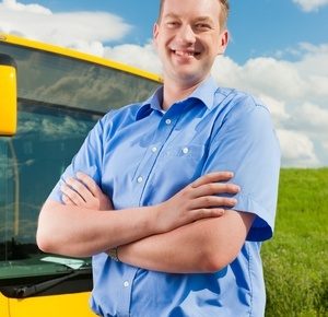 a busdriver standing by his bus smiling with his arms crossed