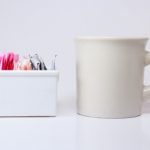 colored sweetener packets in a white ceramic holder with a white coffee mug next to it