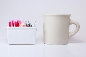colored sweetener packets in a white ceramic holder with a white coffee mug next to it