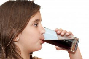 a young girl drinking a glass of cola