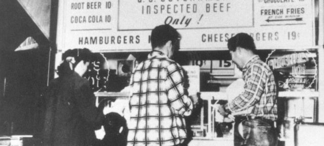 a black and white picture of 2 men at a food counter