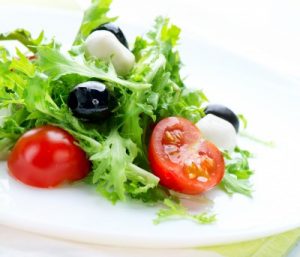 a plate of salad with an olive and a cut tomato
