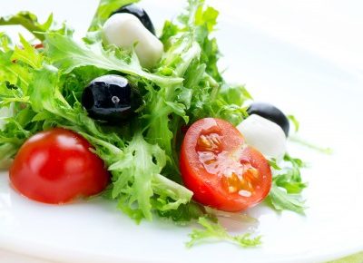 a plate of salad with an olive and a cut tomato