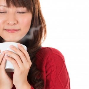 an asian girl in a red dress drinking a white cup of hot tea