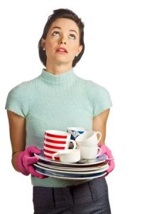 tired white woman holding a stack of dirty dishes iwth dish gloves on