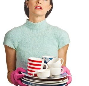 tired white woman holding a stack of dirty dishes iwth dish gloves on