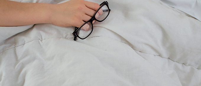 a woman asleep amid white sheets and she's holding her glasses in her hand