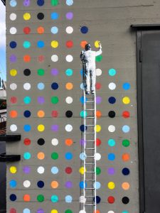 a main on a ladder painting colored dots on a wall