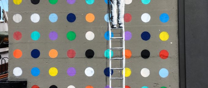 a main on a ladder painting colored dots on a wall
