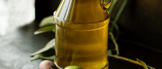 a beautiful bottle of fresh olive oil with big green olives aritting around it on a wooden table