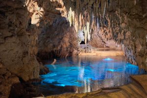 a cave with a beautiful blue lake and stalactites hanging from the ceiling. 